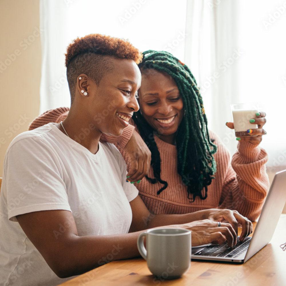 Two people smiling together while looking at a laptop during an LGBTQIA+ screening conversation