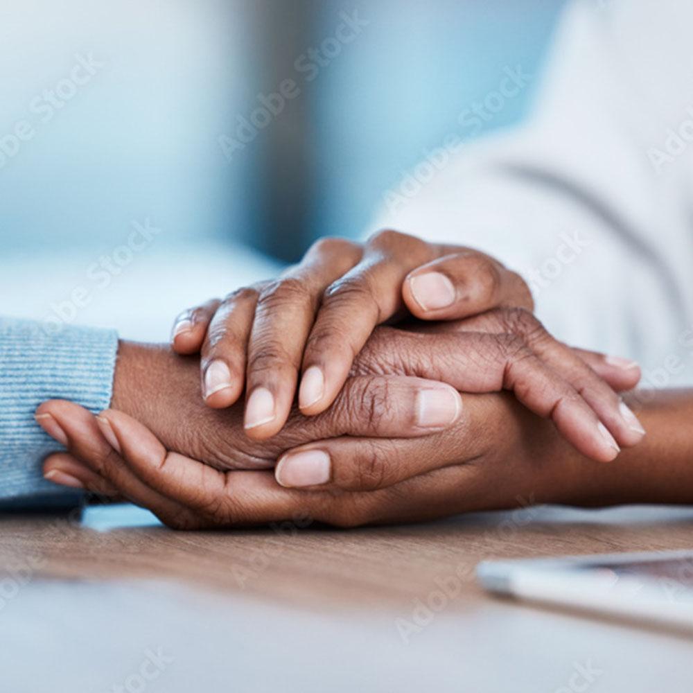 Two hands clasped together in a gesture of comfort and support during cancer treatment
