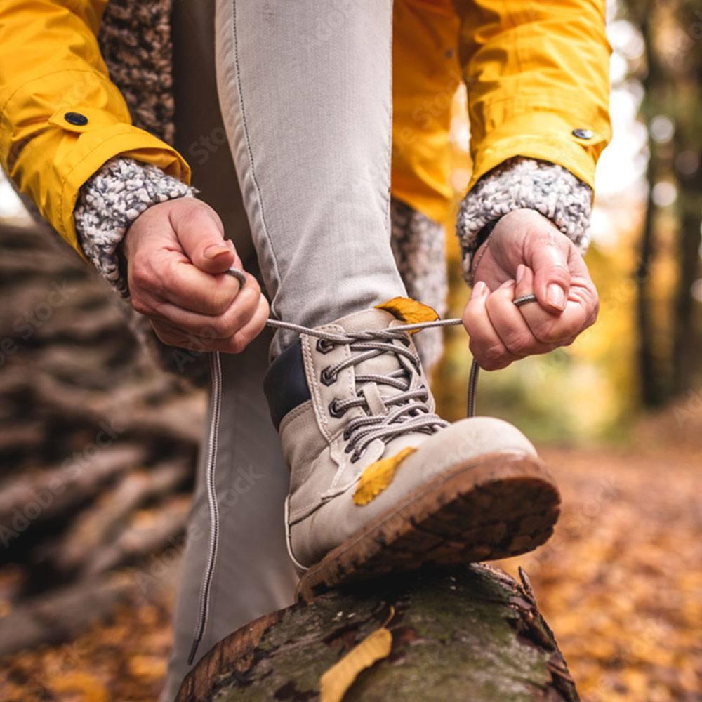 Person tying a hiking boot outdoors while focusing on healthier habits