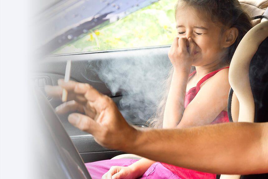 Child holding her nose because of secondhand smoke while her parent smokes in the car