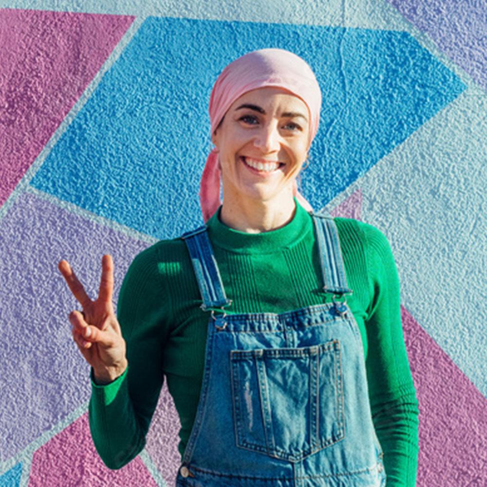 Woman wearing a pink headscarf smiling in front of a colorful mural