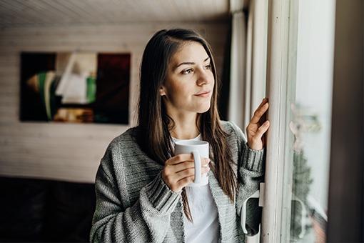 Woman looking outside with a cup of coffee.